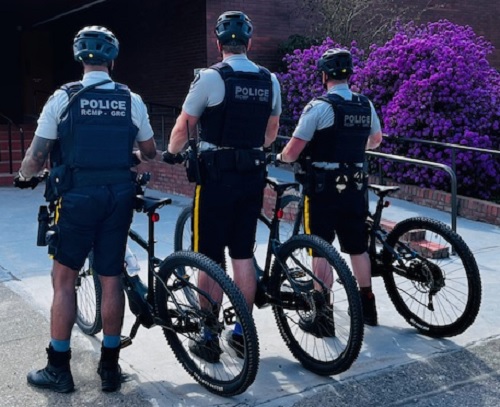 View of the back of three mounties, each with a bicycle and wearing bike helmets.