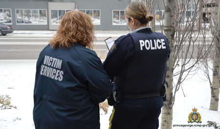 Photo of a Victim Services Employee and a police officer looking at a notebook together. Their backs are to the camera.