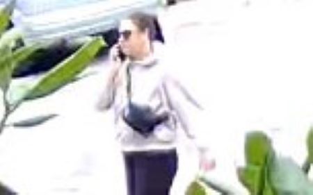 An image of the suspect talking on a cellphone, partially blocked by a green plant.