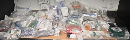 Des dizaines de sacs de preuves transparents remplis de drogues et d’objets divers sur un bureau.