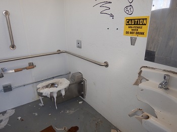 barthroom with broken sink, plugged toilet and graffitied wall