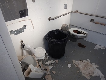 Second bathroom with broken sink and floor littered with toilet paper and paper towell