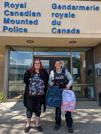 Lori Beech presenting Cst Cooke with backpacks in front of the Fort St John RCMP detachment