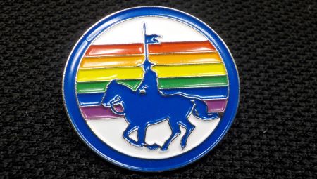 A round pin with a blue silhouette of a horse and rider with a rainbow in the background.  