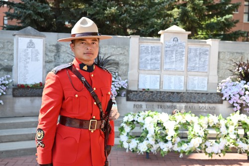 Sous le soleil de Regina, le s.-m.é. m. David Douangchanh, en tunique rouge, est photographié à côté d’un monument commémoratif de la GRC, où sont inscrits les noms des agents décédés.
